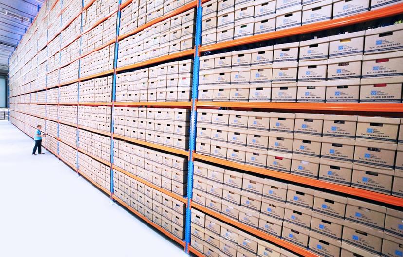 Shop staffer pulling a paper job file from a wall of archived record binders
